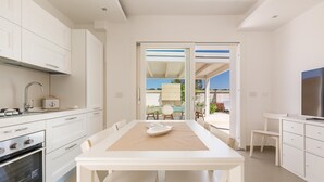 Uma cozinha moderna com armários brancos, uma ilha central e uma área de jantar com mesa e cadeiras.