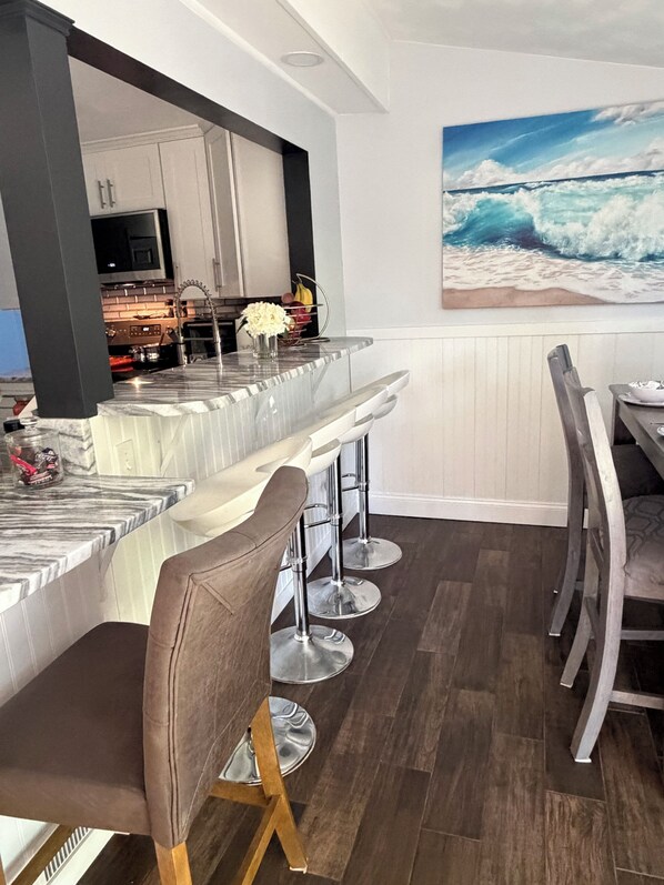 A modern kitchen with a bar area, wooden flooring, and a painting of a beach scene.