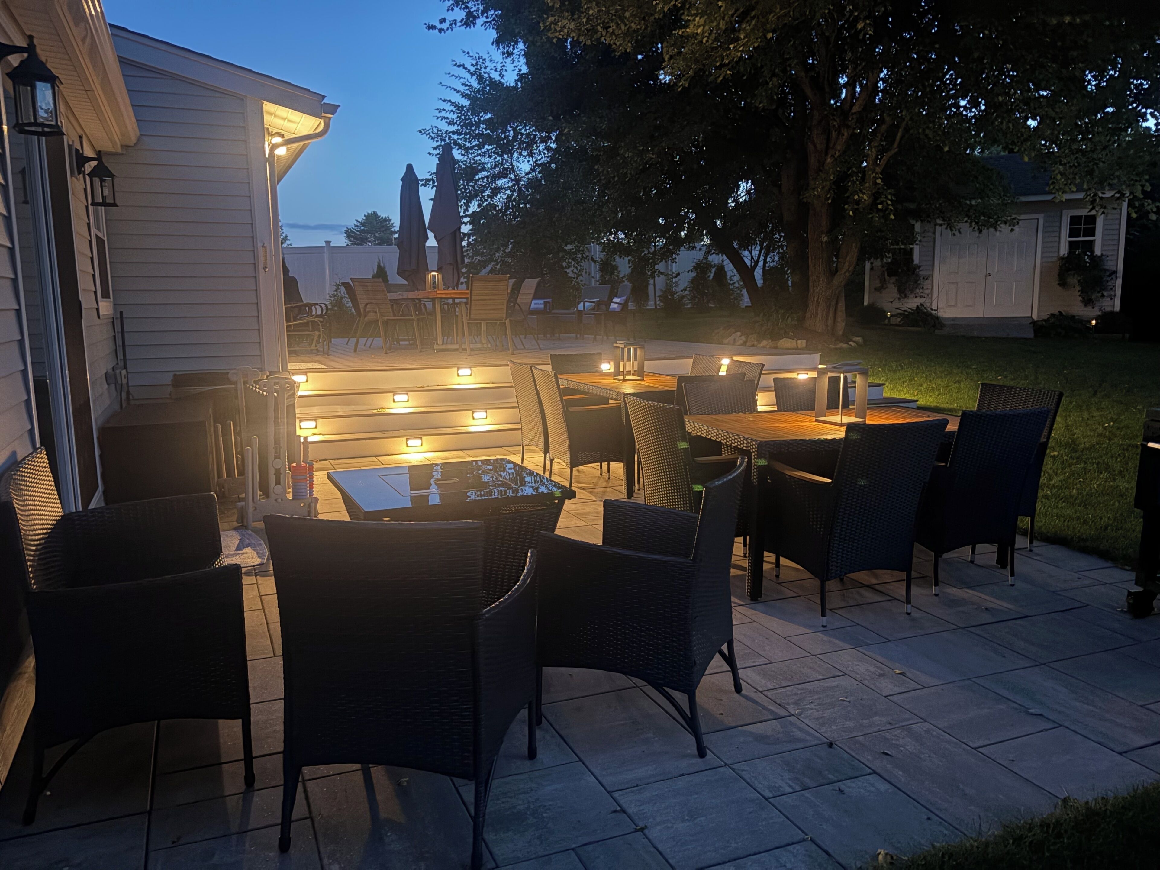 An outdoor patio with multiple tables and chairs, illuminated by overhead lights.