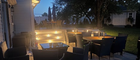 An outdoor patio with multiple tables and chairs, illuminated by overhead lights.