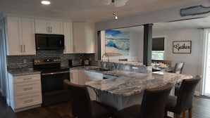 Cozinha moderna com armários brancos, micro-ondas preto, uma ilha grande com banquetas e um quadro de uma onda na parede.