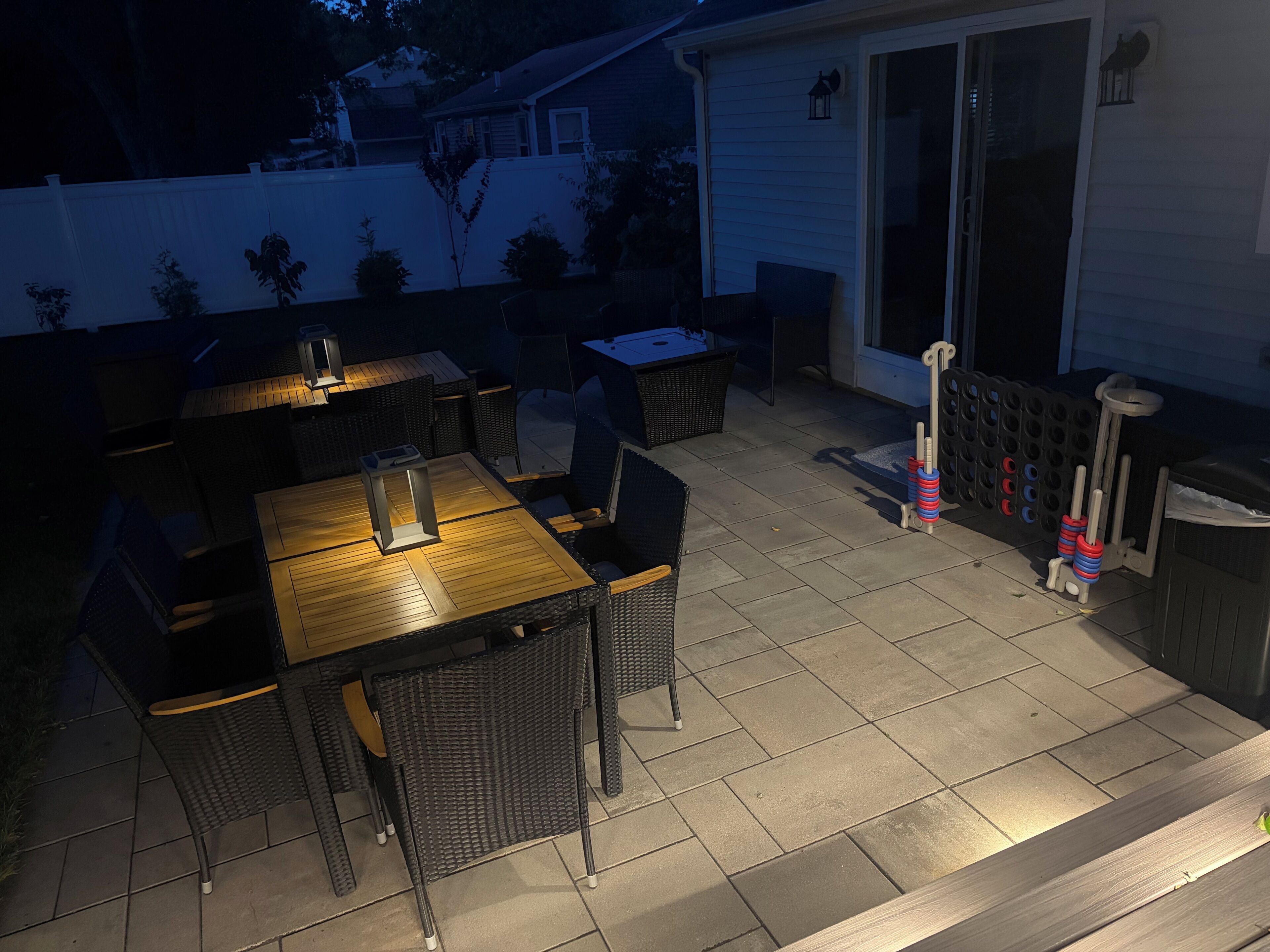 Un espace extérieur aménagé en terrasse, avec une table et des chaises en bois, une petite table avec une lampe, et un panier de basket.