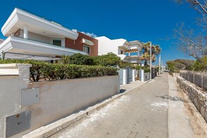 A residential street with modern houses, a clear sky, and a stone wall on one side.