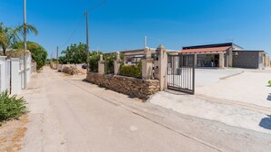 A gated entrance to a property with a paved driveway, a stone wall, and a building with a red roof. - 3047 Villetta Nicols by Barbarhouse (Torricella)
