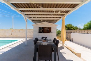 An outdoor dining area with a pool, covered patio, and a small white building with a window. - 3047 Villetta Nicols by Barbarhouse (Torricella)