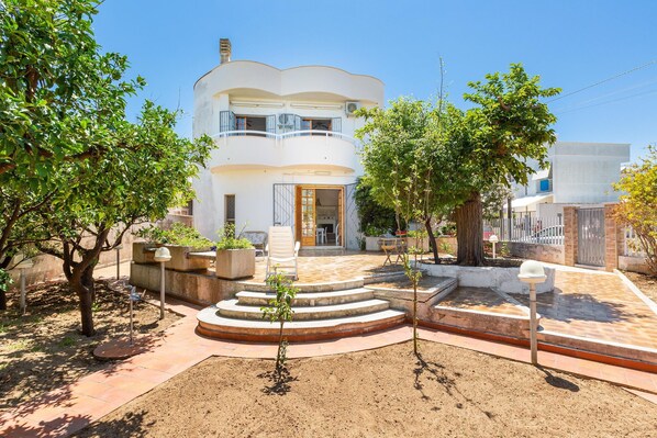 A two-story building with a balcony, a patio area with steps, and a garden with trees and plants. - 2064 Villa Stella Blu by Barbarhouse (Manduria)