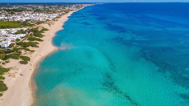 Eine Luftaufnahme einer Küstenlandschaft mit einem Sandstrand und klarem, blauem Wasser.