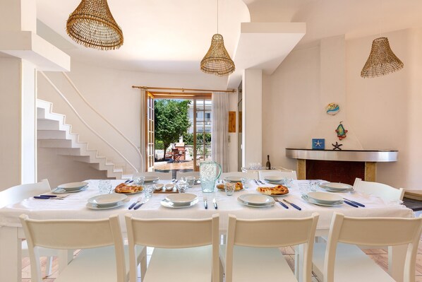 A dining area with a white table set for six, white chairs, and a staircase leading to an outdoor area.