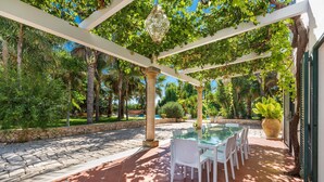 An outdoor patio with a glass-top table and white chairs, surrounded by stone walls and greenery.