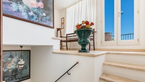 A staircase with a vase of flowers on the landing, a framed painting above, and a view of the sky through a window.