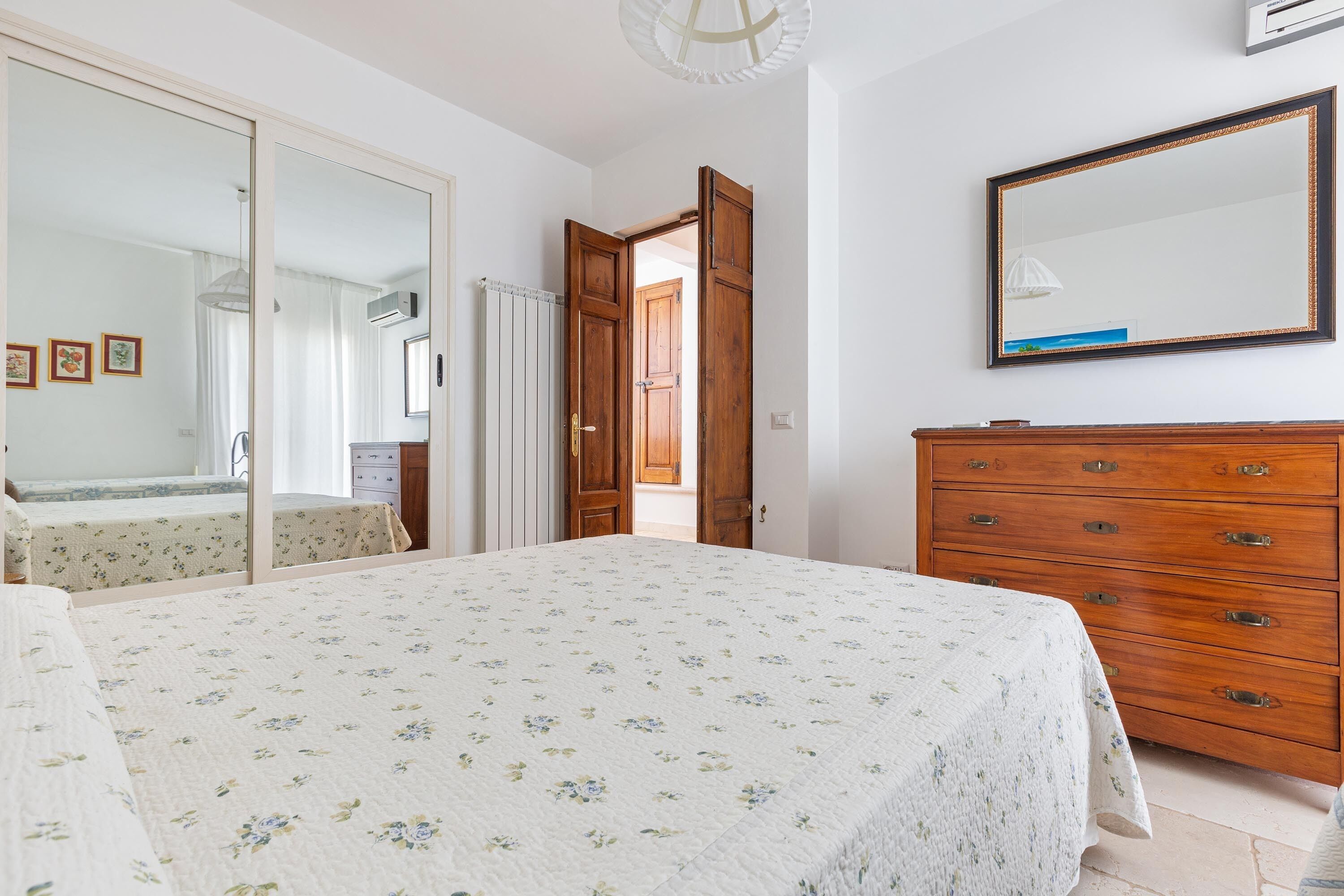 A bedroom with a bed, a dresser, a mirror, and a door leading to another room.