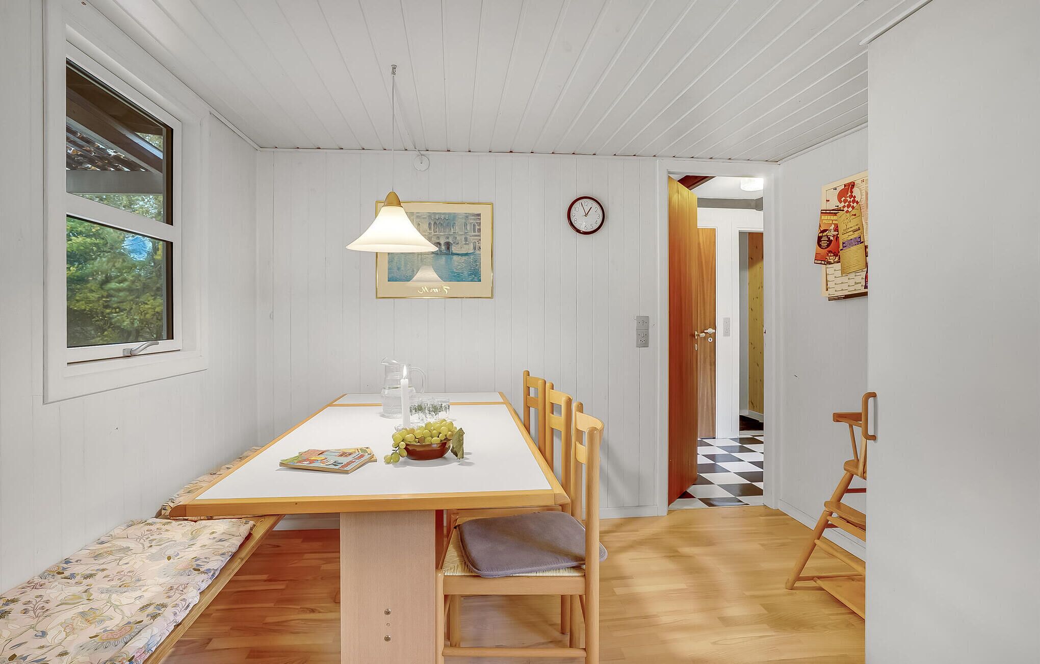 Uma sala de jantar com uma mesa de madeira, cadeiras, um abajur, um relógio e um quadro na parede.