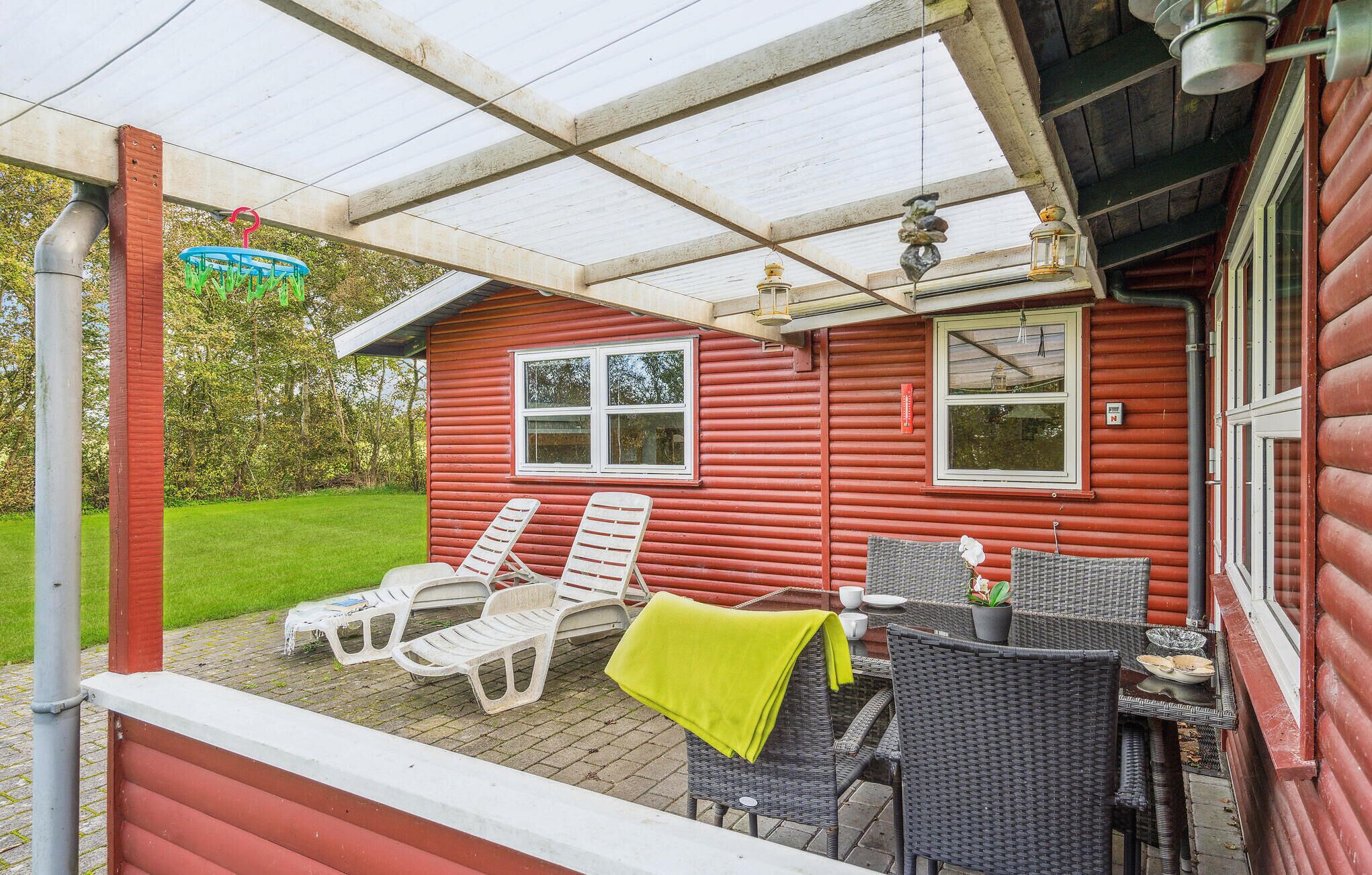 A red wooden house with a covered patio, white plastic chairs, wicker furniture, and a table with a yellow cloth.