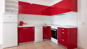 A kitchen with red cabinets, a white refrigerator, a dishwasher, and a stove.