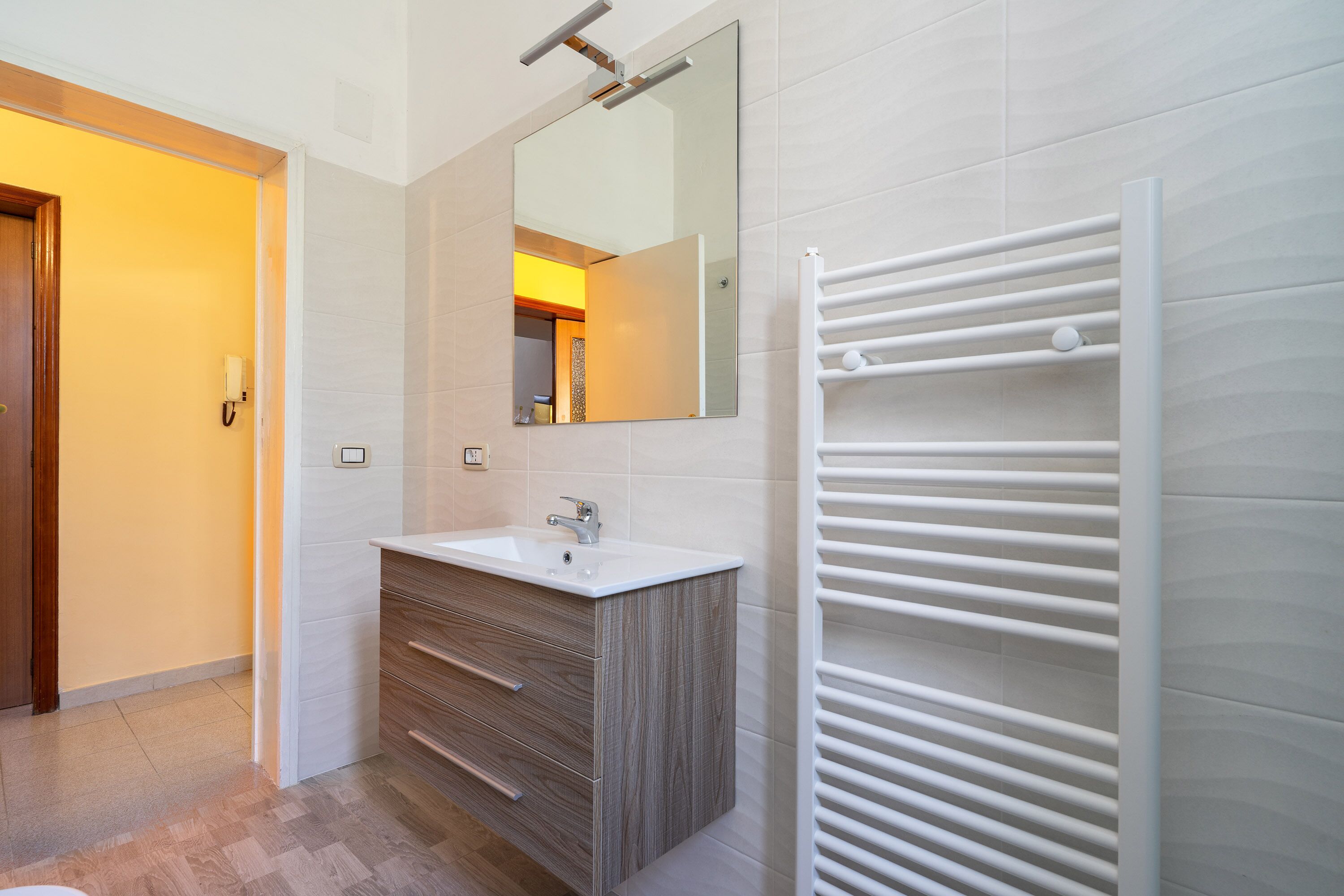 Ein modernes Badezimmer mit einem weißen Waschbecken, einem Holz-Waschtisch, einem großen Spiegel und einem weißen Handtuchhalter.