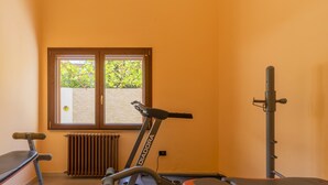 Een sportschool met fitnessapparatuur, een bank en een raam met uitzicht op groen.