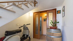 Een gang met een scooter langs de muur, een houten vat en een houten trap.