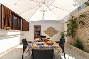 An outdoor patio with a table set for dining, surrounded by wicker chairs, under a large umbrella.