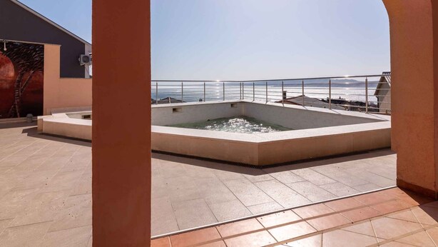 Una piscina en la azotea con vistas despejadas al mar, rodeada por una terraza de baldosas y una barandilla metálica.