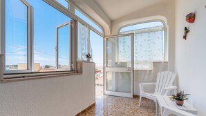 A balcony with a white chair, a small table with a potted plant, and a sliding glass door leading to an outdoor area.