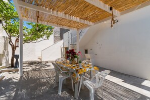 An outdoor patio with a table set for dining, surrounded by white plastic chairs, under a wooden pergola. - 3057 Villa Perla Marina- Appartamento PP by Barbarhouse (Torricella)