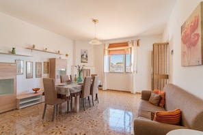 A dining area with a table set for four, a sofa, and a window with curtains.
