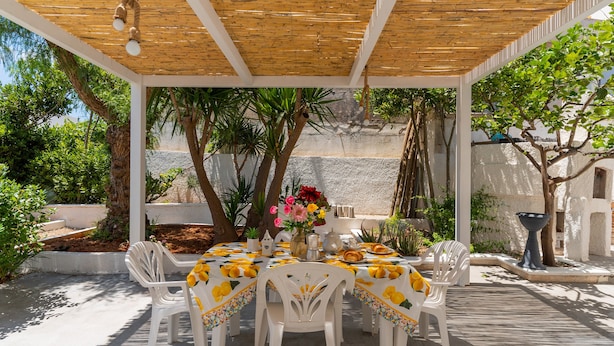 A covered outdoor dining area with white plastic chairs and a table set with a yellow tablecloth.