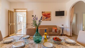 A dining area with a table set for four, a vase with flowers, and a bowl of fruit.