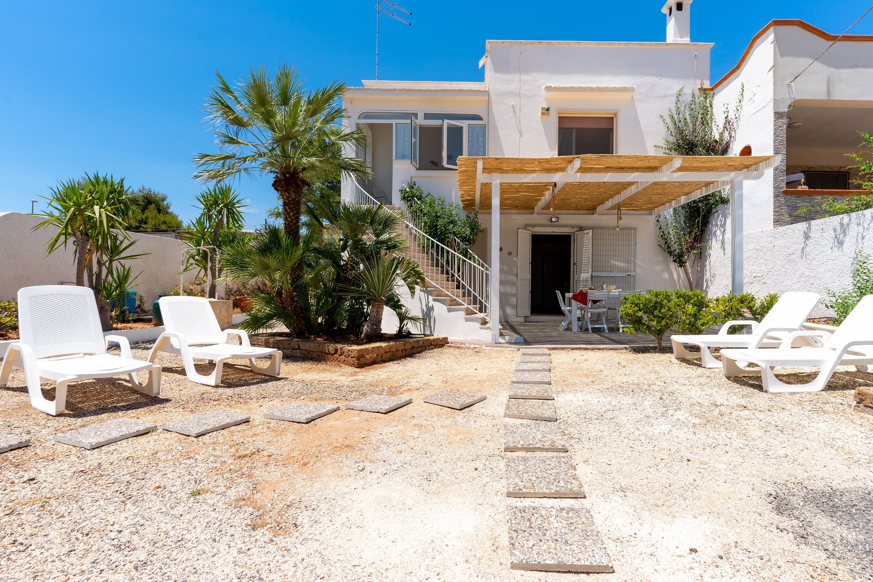 A modern house with a covered patio, outdoor seating, and a staircase leading to the entrance.