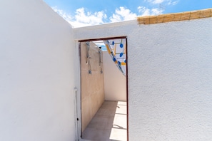 A narrow hallway with a tiled floor leading to a bathroom with a shower and a towel rack.
