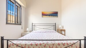 Ein Schlafzimmer mit einem Bett, einem Nachttisch, einer Lampe, einem Gemälde und einem Fenster.
