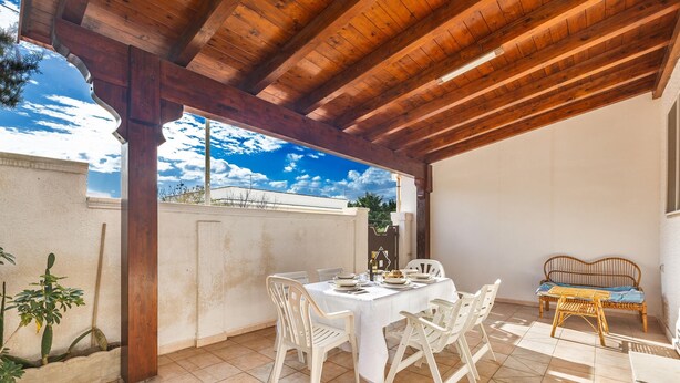 Eine Terrasse im Freien mit einer Holzw pergola, einem weißen Esstisch und einem Korbsessel-Sofa.