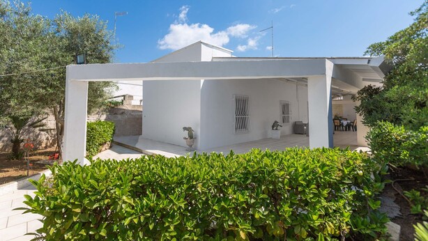 A modern white house with a covered patio area, outdoor seating, and a well-maintained garden. - 3041 Villetta Sunshine by Barbarhouse (Manduria)