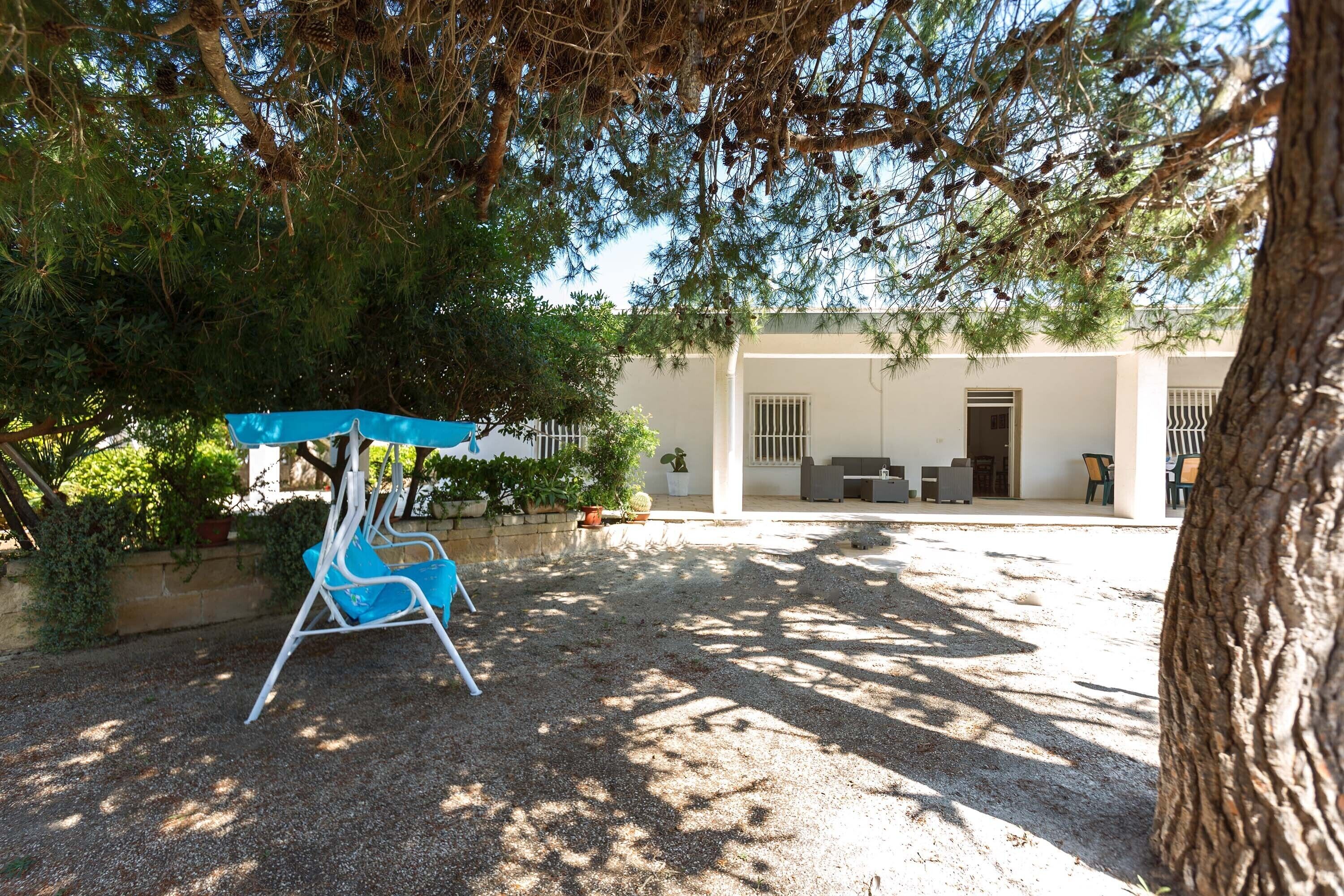 A covered seating area with a swing, a gravel courtyard, and a building with a white exterior and a door.
