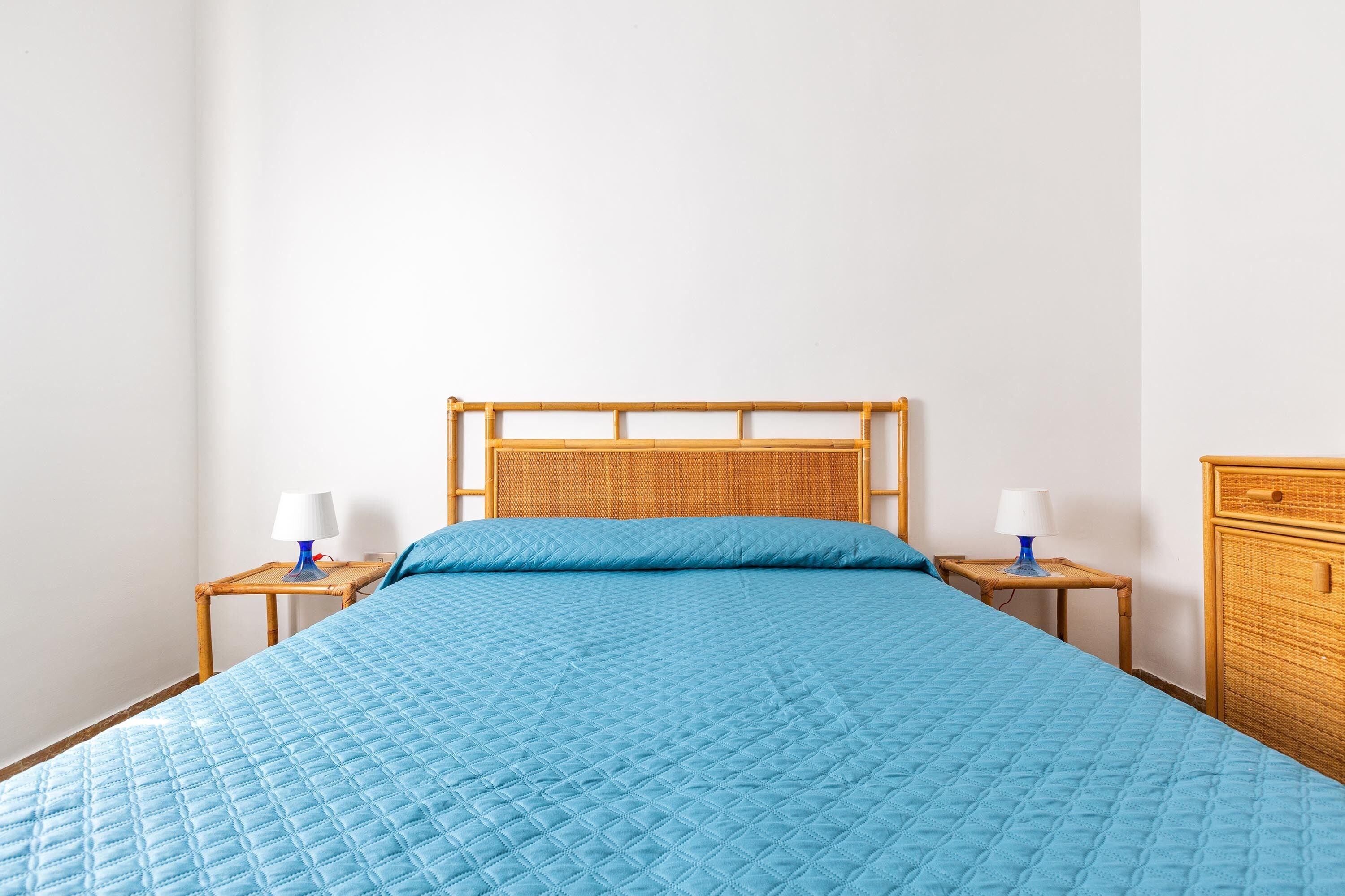A bed with a blue quilt, two bedside tables with lamps, and a wooden headboard.