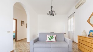 Un salon avec un canapé gris, une commode en bois, un parquet à motifs, un lustre et un miroir au mur.