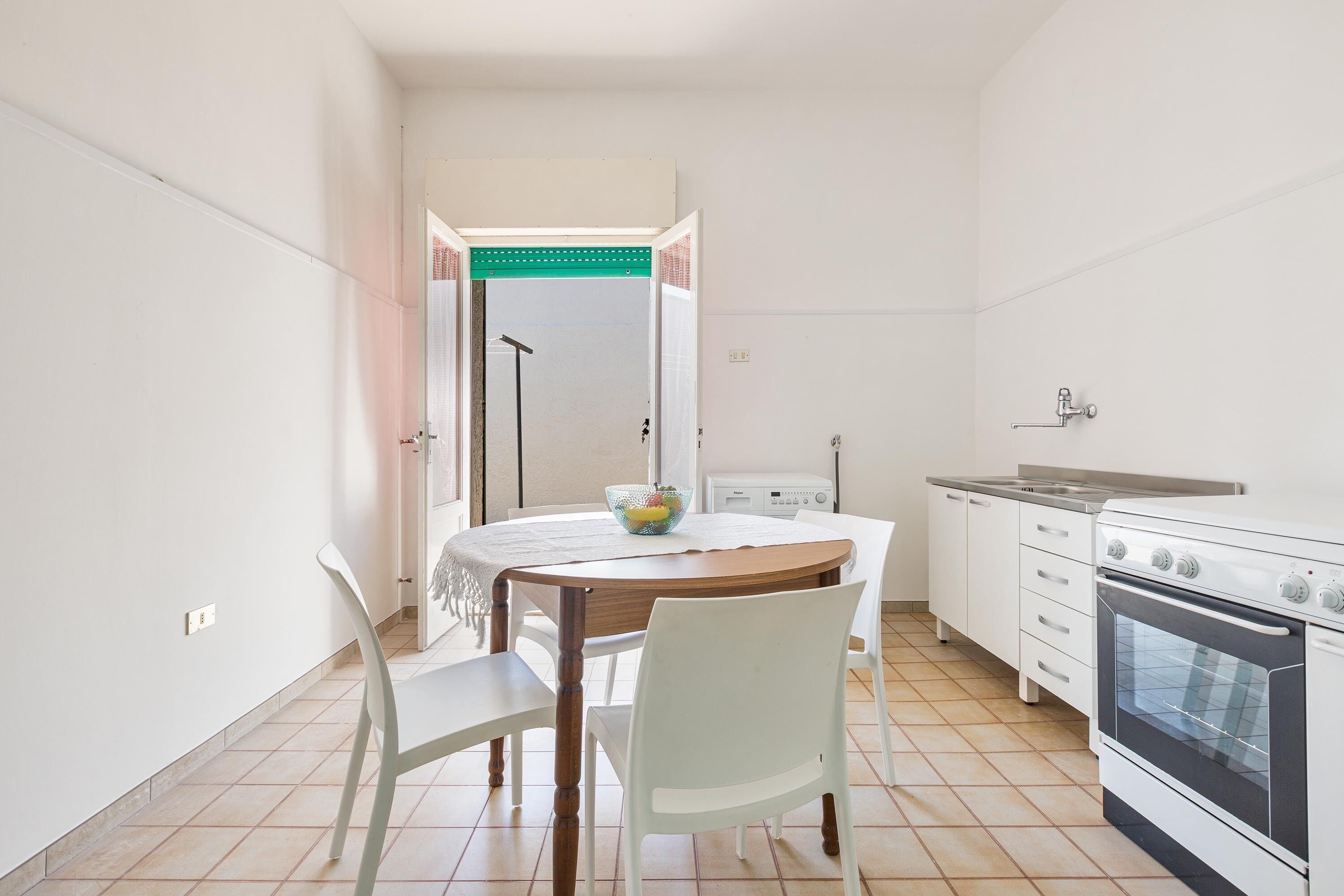 Een kleine keuken met witte kastjes, een fornuis en een eettafel met stoelen.