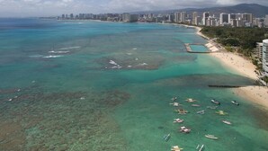 An aerial view of a coastal city with a beach, clear turquoise waters, and numerous boats.