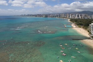 Vista aérea de uma cidade costeira com praia, águas azuis cristalinas e diversos barcos.