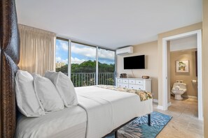 Relax in a spacious room with a large bed, flat-screen TV, and a balcony offering a view of the city and greenery.