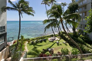 Relax in a serene outdoor space with lounge chairs, tables, and a lush lawn surrounded by palm trees and offering scenic ocean views.