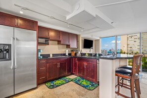 Cozinha moderna com eletrodomésticos de aço inoxidável, armários de madeira e uma grande janela com vista para a cidade.