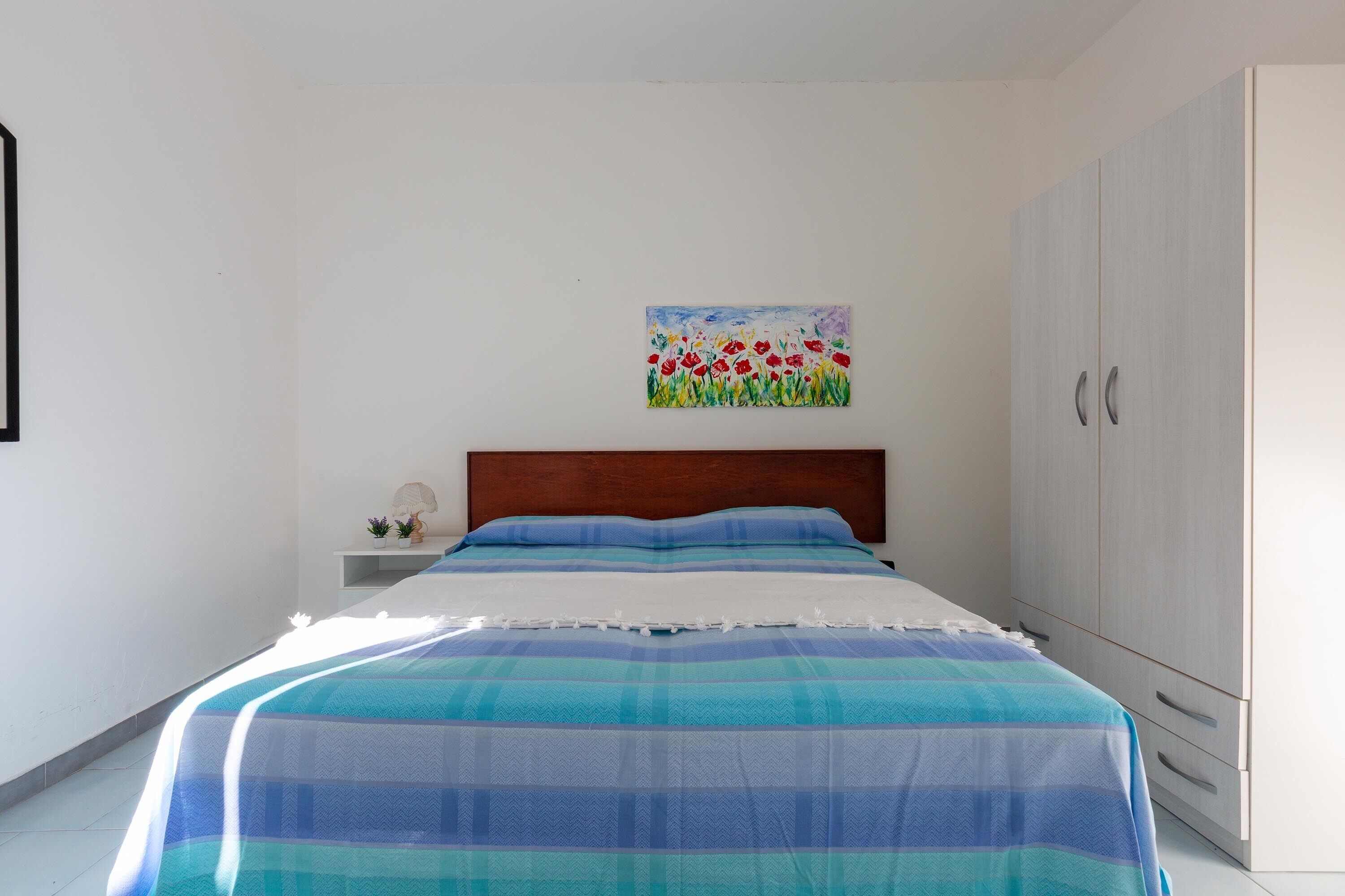 A bedroom with a bed, a nightstand, a painting, and a wardrobe.