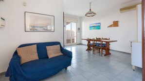 A living room with a blue sofa, a dining table with chairs, and a ceiling fan. - 2686 Villetta Fiore di Maggio by Barbarhouse (Porto Cesareo)