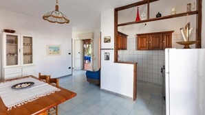 A kitchen with wooden cabinets, a dining table with a lace tablecloth, and a hanging light fixture. - 2686 Villetta Fiore di Maggio by Barbarhouse (Porto Cesareo)