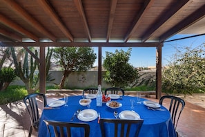 A covered outdoor dining area with a blue tablecloth, set for four people.