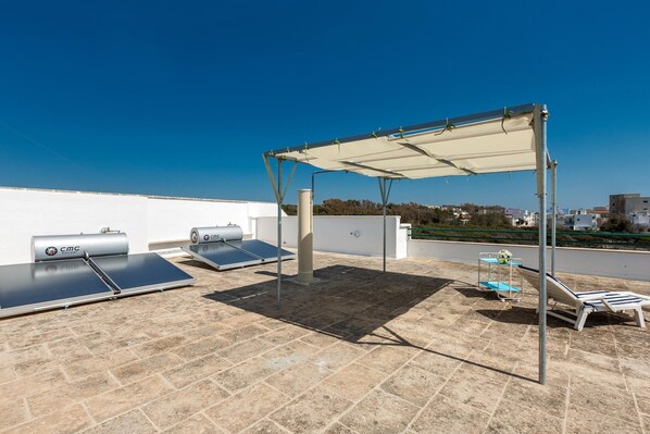 Une terrasse sur le toit équipée de panneaux solaires, d’une pergola et de chaises longues.