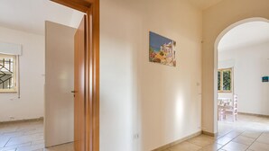 An open hallway with tiled flooring, a wooden door, a wall-mounted painting, and an archway leading to another room. - 2679 Villetta Filomena - Appartamento Leo by Barbarhouse (Manduria)