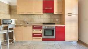 A modern kitchen with wooden cabinets, a red oven, and a microwave. - 2679 Villetta Filomena - Appartamento Leo by Barbarhouse (Manduria)