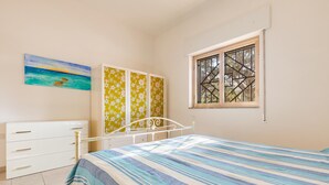A bedroom with a bed, a dresser, a window with bars, and a painting on the wall. - 2679 Villetta Filomena - Appartamento Leo by Barbarhouse (Manduria)